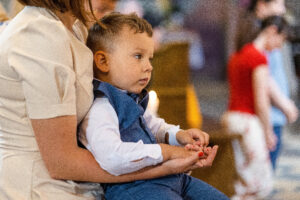 chlopczyk siedzi spokojnie u mamy na rekach w kosciele w zielonce