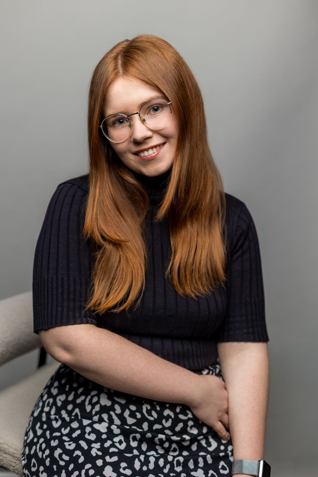 Uśmiechnięta rudowłosa kobieta w okularach, naturalny portret biznesowy zrealizowany w studio.